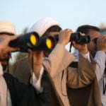 three men using binoculars